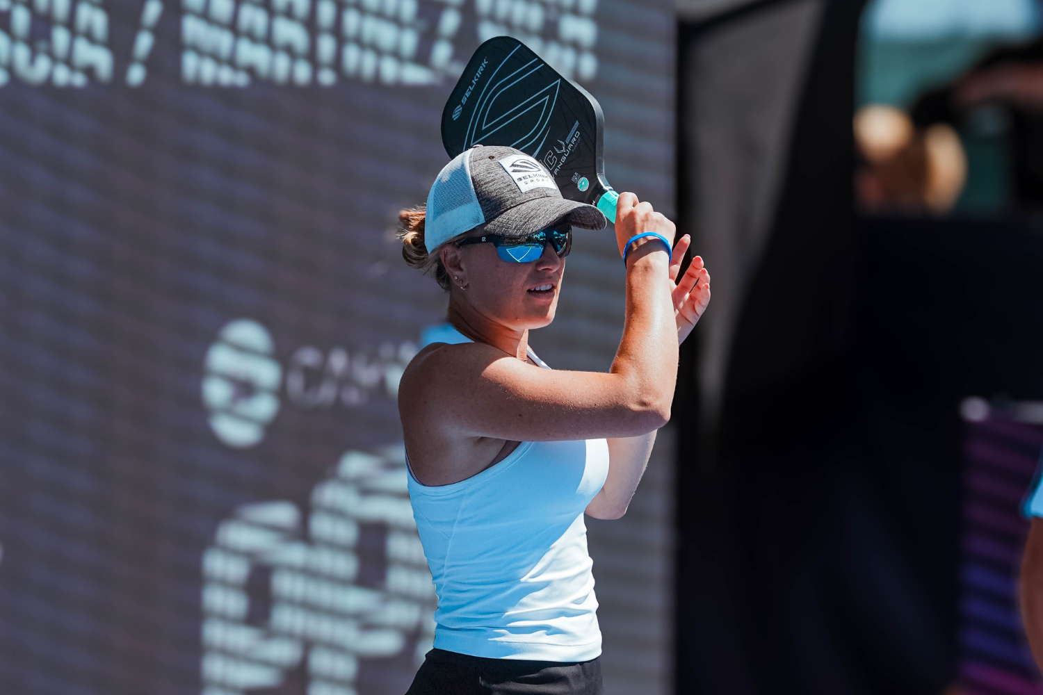 Female pickleball player wearing sunglasses and cap, focused on incoming ball.