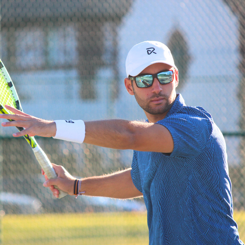 Golfer wearing RIA cap and sunglasses swinging golf club against clear blue sky