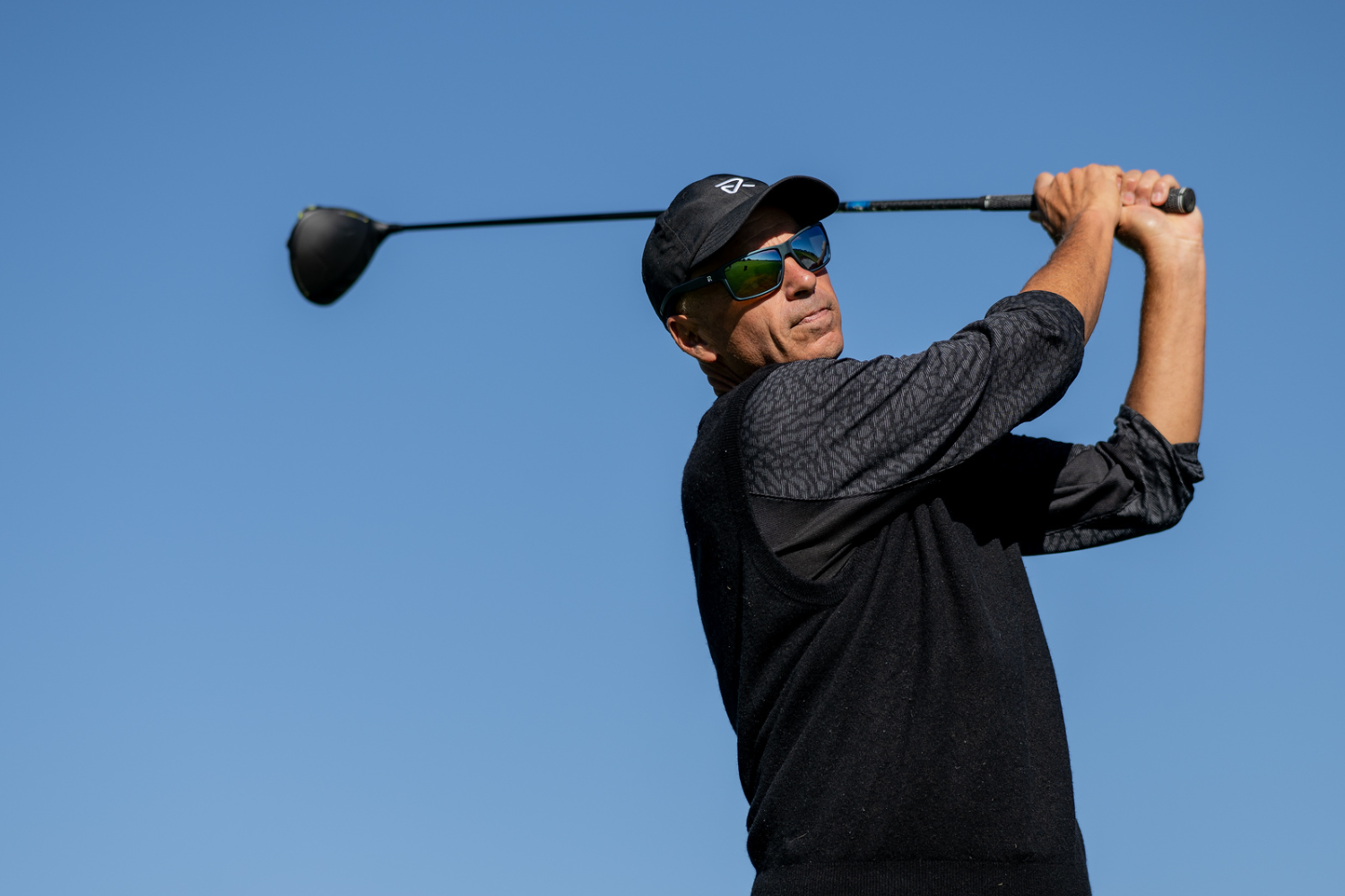 Man in purple sweater and gray beanie swinging golf club against clear sky
