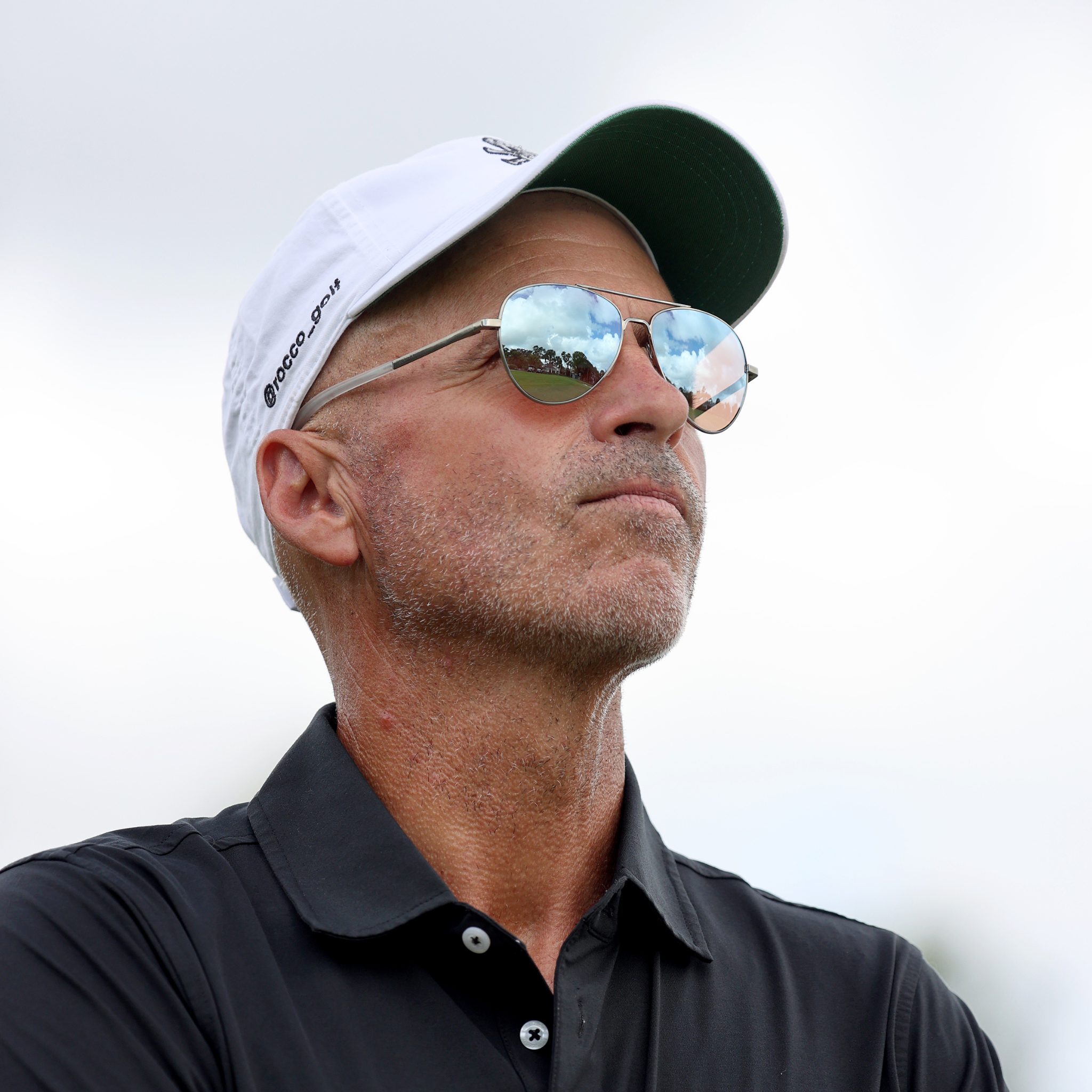 Rocco Mediate wearing a white cap and RIA Eyewear sunglasses with a sky background