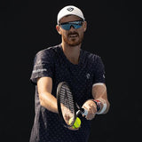 Male tennis player in dark shirt and white cap preparing to serve with racket and ball.