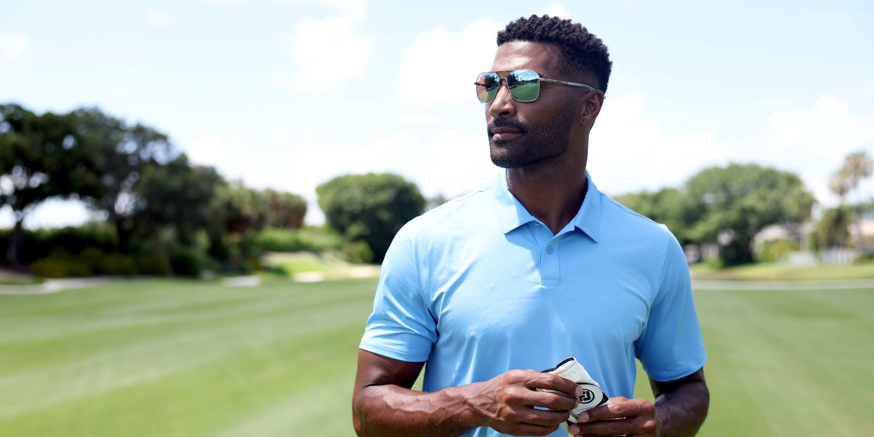 Man in a light blue polo shirt and sunglasses holding a golf club on a golf course with titanium sunglasses.